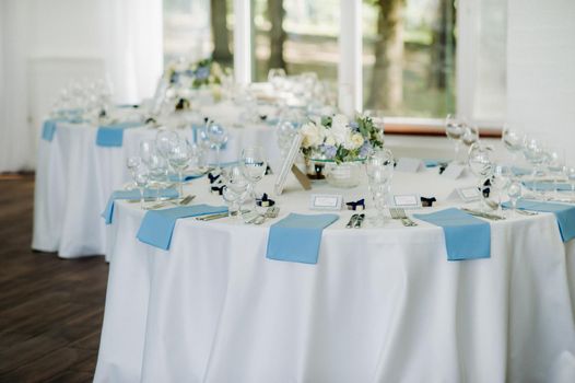 The festive table is decorated in light colors with blue napkins and flowers without food.