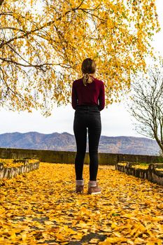 Autumn leaves fallen on alone woman walking on the autumn alley. Autumn landscape, orange foliage in a park in Orsova, Romania, 2020