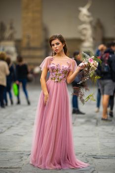 A bride in a pink dress with a bouquet stands in the center of the Old City of Florence in Italy.