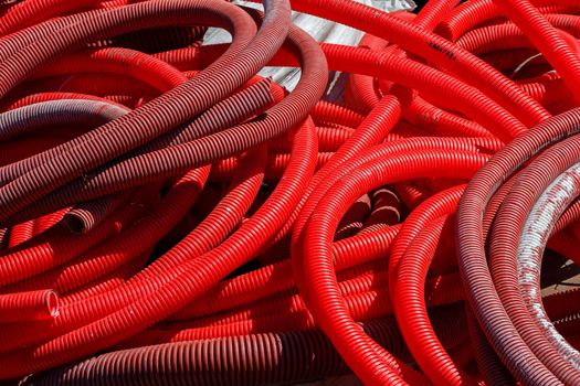 a pile of red corrugated PVC pipes for cable lay on the construction site, full frame background