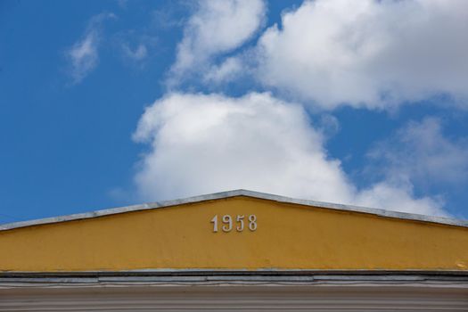 close-up view of yellow roof ridge wit digits 1958 on blue sky with white clouds background.