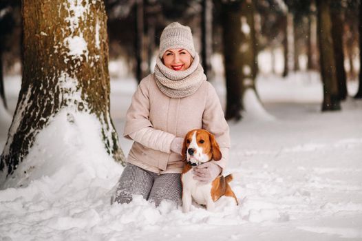 a woman on a winter day with her pet dog beagle in the winter forest playing.