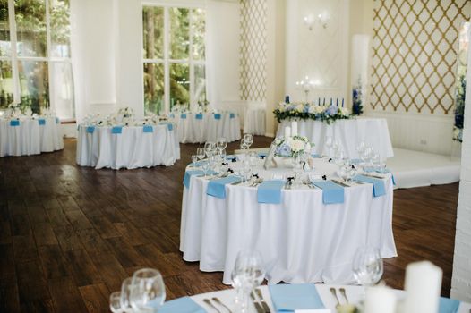 The festive table is decorated in light colors with blue napkins and flowers without food.