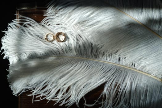 Two wedding rings lie in white feathers. The concept of love.