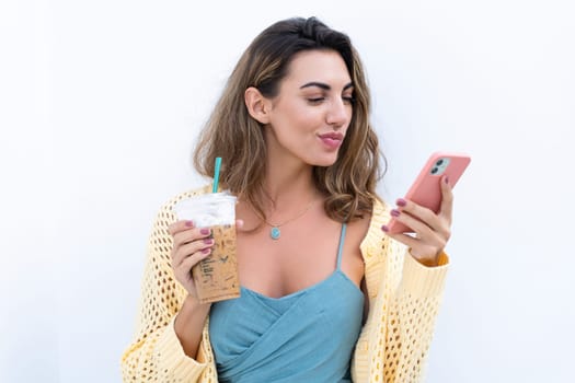 Portrait of beautiful woman in green summer dress on white background natural daylight, holding iced coffee cappuccino and phone thoughtful smiling