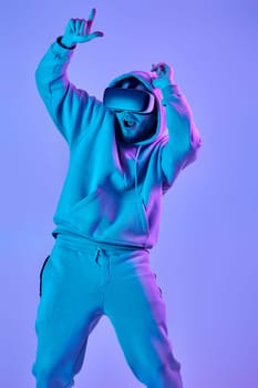 man in sweatshirt using virtual reality glasses and playing video games on blue background. Neon lighting