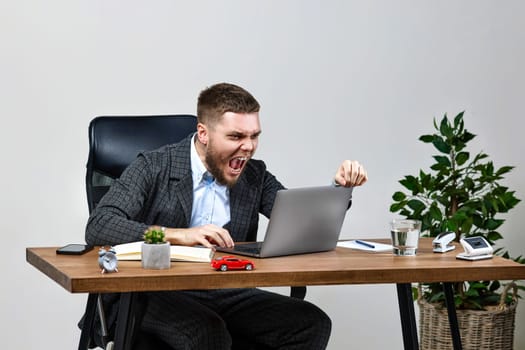 angry businessman shouting loudly, sitting on chair at deskand having computer problems or virus attack