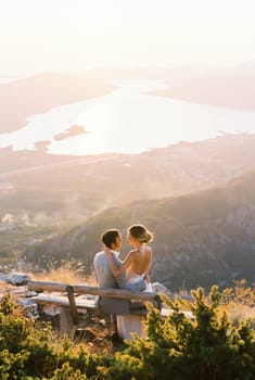 Bride sits on the lap of groom on a bench on top of a mountain. High quality photo