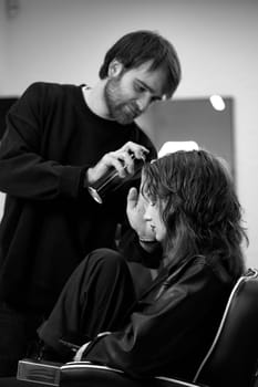 male hairdresser fixing hair of young woman with hairspray in hair salon.