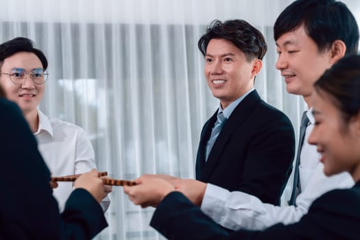 Closeup hand holding wooden gear by businesspeople wearing suit for harmony synergy in office workplace concept. Group of people hand making chain of gears into collective form for unity symbol.