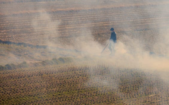 Smoke rises around masked man during controlled burn on dry fields at farm. High quality photo