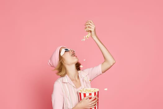 pleased blonde woman in t-shirt and hat eating popcorn on pink background.