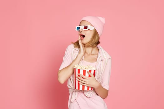 amazed woman holding bucket of popcorn and looking at the side on pink background