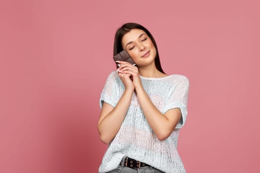 lovely smiling dreamy woman enjoying dark chocolate isolated on pastel pink background