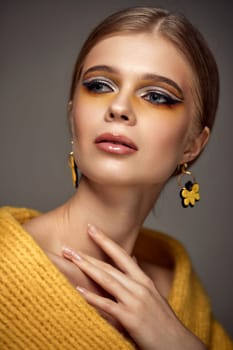 Beauty blonde model girl with fashionable creative make-up and yellow earrings. . Creative yellow eye makeup ideas.