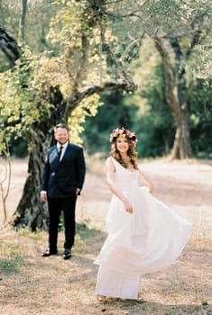 Bride twirling in white toga dress in front of groom in park. High quality photo
