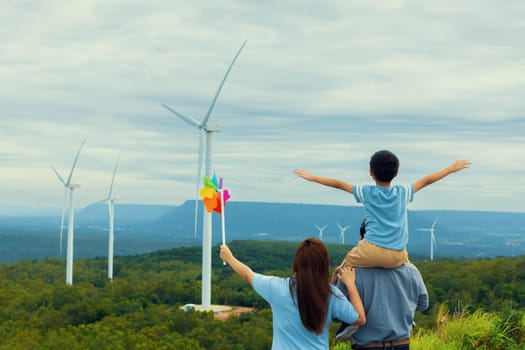 Progressive happy family enjoying their time at wind farm for green energy production concept. Wind turbine generators provide clean renewable energy for eco-friendly purposes.
