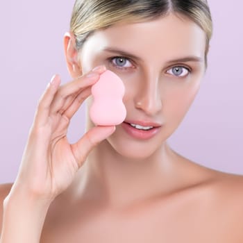 Closeup alluring beautiful female model applying powder puff for facial makeup concept. Portrait of flawless perfect cosmetic skin woman put powder foundation on her face in pink isolated background.