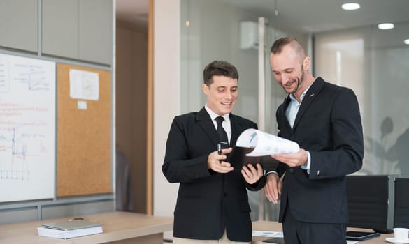 Two business people talk project strategy at office meeting room. Businessman discuss project planning with colleague at modern workplace while having conversation and advice on financial data report...