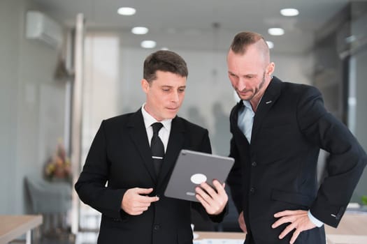 Two business people talk project strategy at office meeting room. Businessman discuss project planning with colleague at modern workplace while having conversation and advice on financial data report...