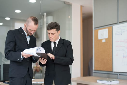 Two business people talk project strategy at office meeting room. Businessman discuss project planning with colleague at modern workplace while having conversation and advice on financial data report...