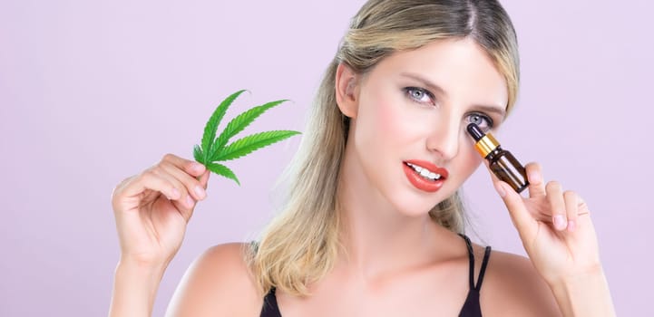 Alluring portrait of beautiful woman with perfect makeup hold green leaf, marijuan extracted bottle for skincare treatment product. Cannabis CBD oil for cosmetic and beauty in pink isolated background
