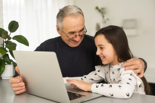 Portrait of senior man and young girl granddaughter using laptop at home