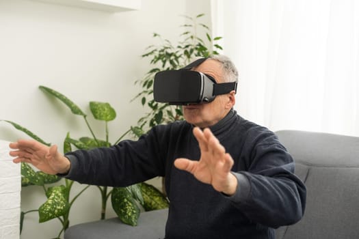 handsome senior man using VR 360 glasses at home. Making browse and tap gestures. Concept of active modern elderly people, learning to use contemporary technologies