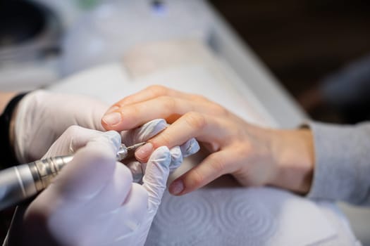 Manicure performed on the natural nail plate. A visit to a professional beauty salon. A woman performs a professional manicure. The manicurist uses disposable gloves.