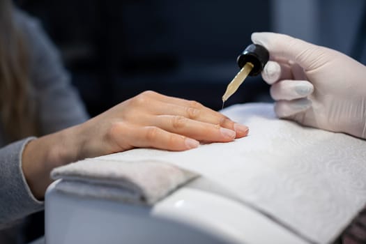 The beautician performs the preparation of the nail plate for further nail care. A beauty salon customer has a manicure done.