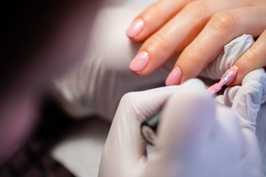 A beautician paints the nail of the index finger. A woman using the services of a manicurist. The beautician paints the client's nails pink. Applying a layer of hybrid varnish.