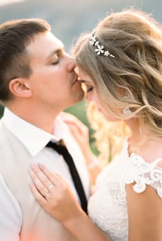 Groom kisses the forehead of bride on the background of the mountains. Portrait. High quality photo