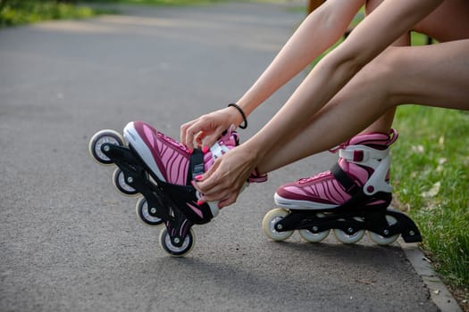 Close-up of a girl's legs putting on rollerblades. Correcting the buckle in rollerblades. The athletic legs of a young person sitting on a park bench. Person in summer short clothing.
