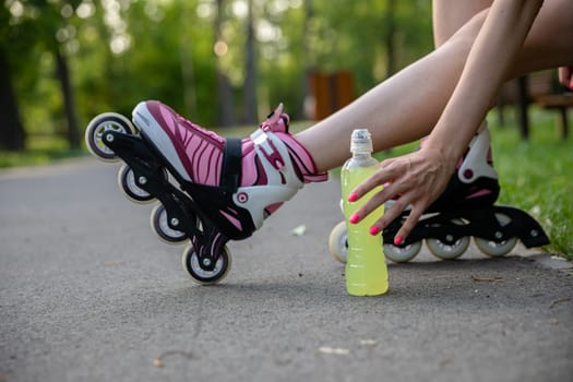 Close-up of the girl's legs visible in profile. A woman sitting on a park bench. Girl on roller skates reaches for isotonic drink. Hydration after a grueling workout.