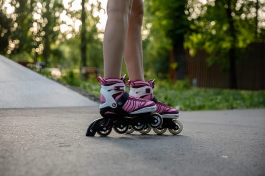 Close-up of a woman's legs. Woman wearing rollerblades. Playing sports in a city park. A girl rollerblades on an asphalt alley. Sports gear in fashionable purple colors.