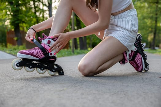A girl dressed in summer sportswear. A woman kneels on one knee. A person putting on rollerblades. Fine-tuning sports equipment before training.