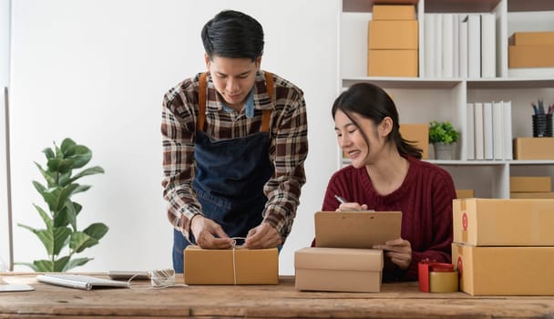Young asian people couple Male and female small business owner checking online orders and packing the product together