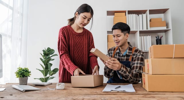 Young asian people couple Male and female small business owner checking online orders and packing the product together