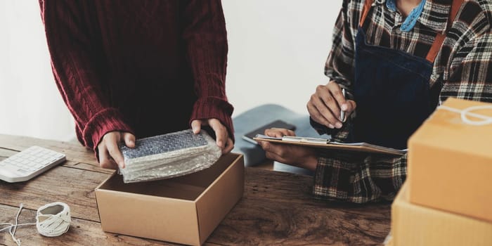 Young asian people couple Male and female small business owner checking online orders and packing the product together