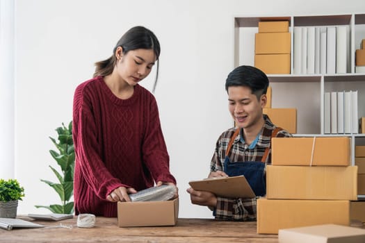 Young asian people couple Male and female small business owner checking online orders and packing the product together