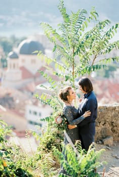 Groom hugs bride in a blue dress on the observation deck above the town. High quality photo