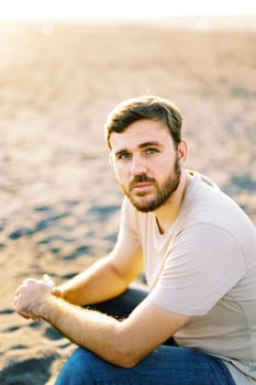 Young man in a t-shirt sits on a sandy beach. High quality photo