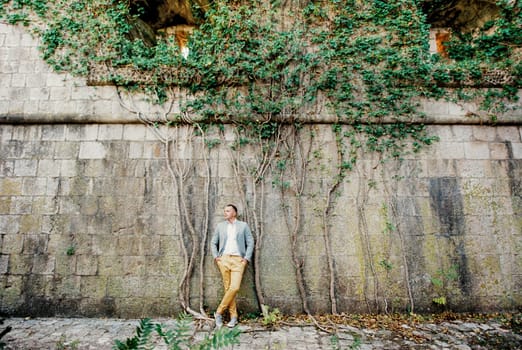 Man in a suit stands near the stone wall of a medieval fortress. High quality photo