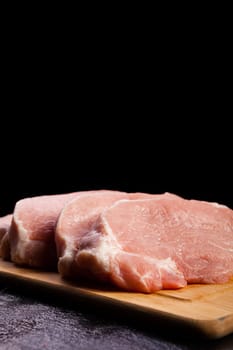 four pieces of fresh raw meat on wooden board on black wooden background. Gourmet food and fresh uncooked meal