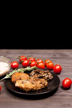 Delicious Pork steak in black plate with grilled mushrooms, oregano cherry tomatoes and bean paste on a wooden table