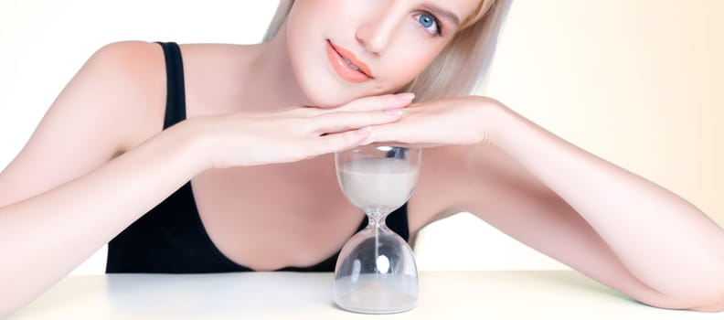 Personable model hold hourglass in aging young beauty concept of anti-aging skincare treatment for woman. Beautiful girl with smooth flawless natural facial skin in isolated background.