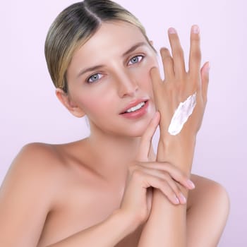 Alluring beautiful woman applying moisturizer cream on her hand for perfect skincare treatment in pink isolated background. Caucasian women portrait with skin rejuvenation and cosmetology concept.