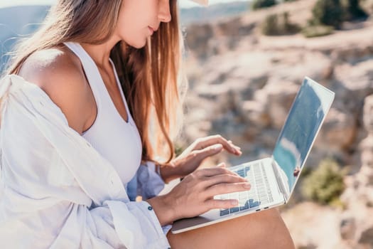 Digital nomad, Business woman working on laptop by the sea. Pretty lady typing on computer by the sea at sunset, makes a business transaction online from a distance. Freelance remote work on vacation