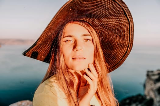 Portrait of happy young woman wearing summer black hat with large brim at beach on sunset. Closeup face of attractive girl with black straw hat. Happy young woman smiling and looking at camera at sea