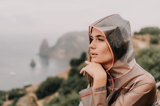 Woman rain park. Happy woman portrait wearing a raincoat with transparent umbrella outdoors on rainy day in park near sea. Girl on the nature on rainy overcast day